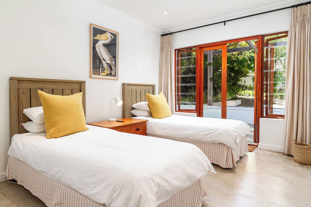 Habitación con dos camas, cabecera de madera, mesita de noche, lámpara y ventana con cortinas.