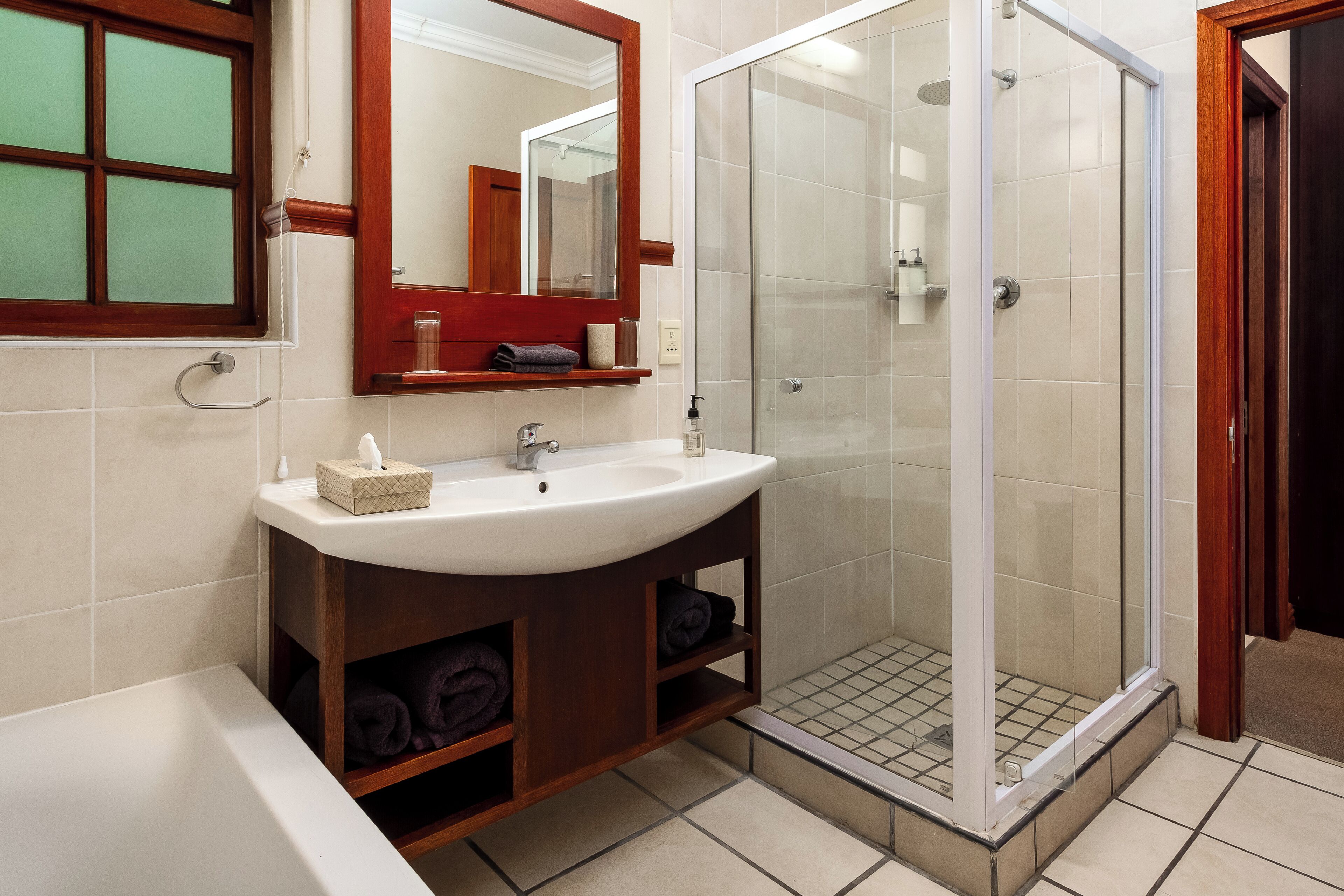 A bathroom with a white sink, a mirror, a glass-enclosed shower, and a wooden vanity.