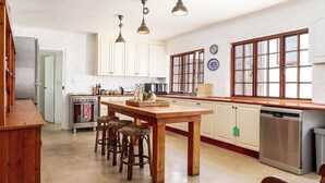 Une cuisine avec des meubles blancs, un îlot central en bois doté de tabourets, des appareils en acier inoxydable et un éclairage suspendu.