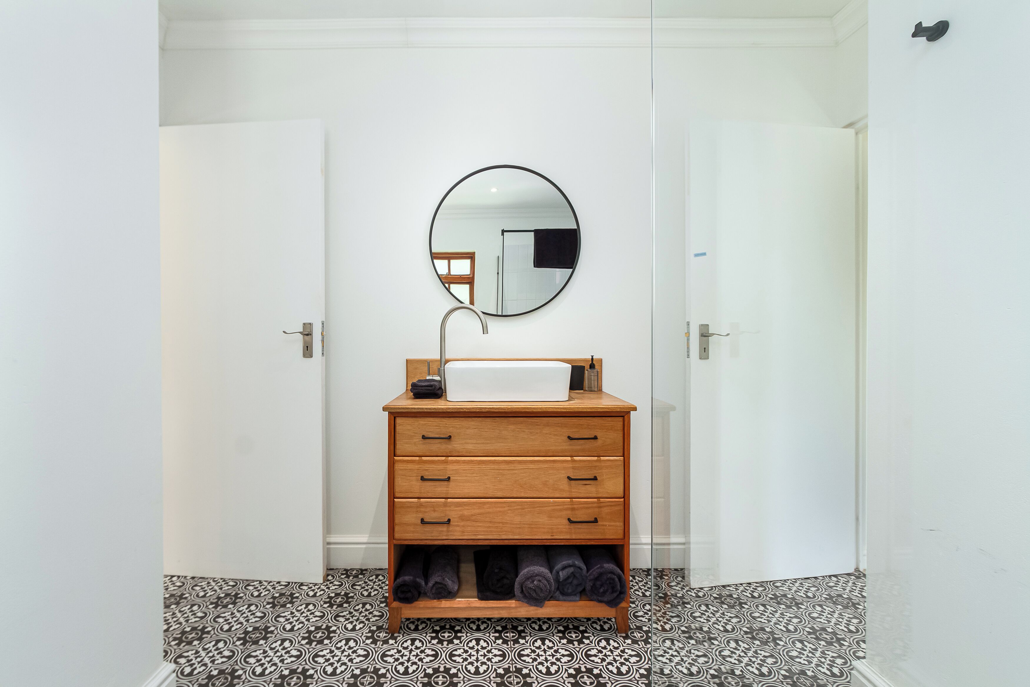 A bathroom with a white sink, wooden vanity, and a round mirror.