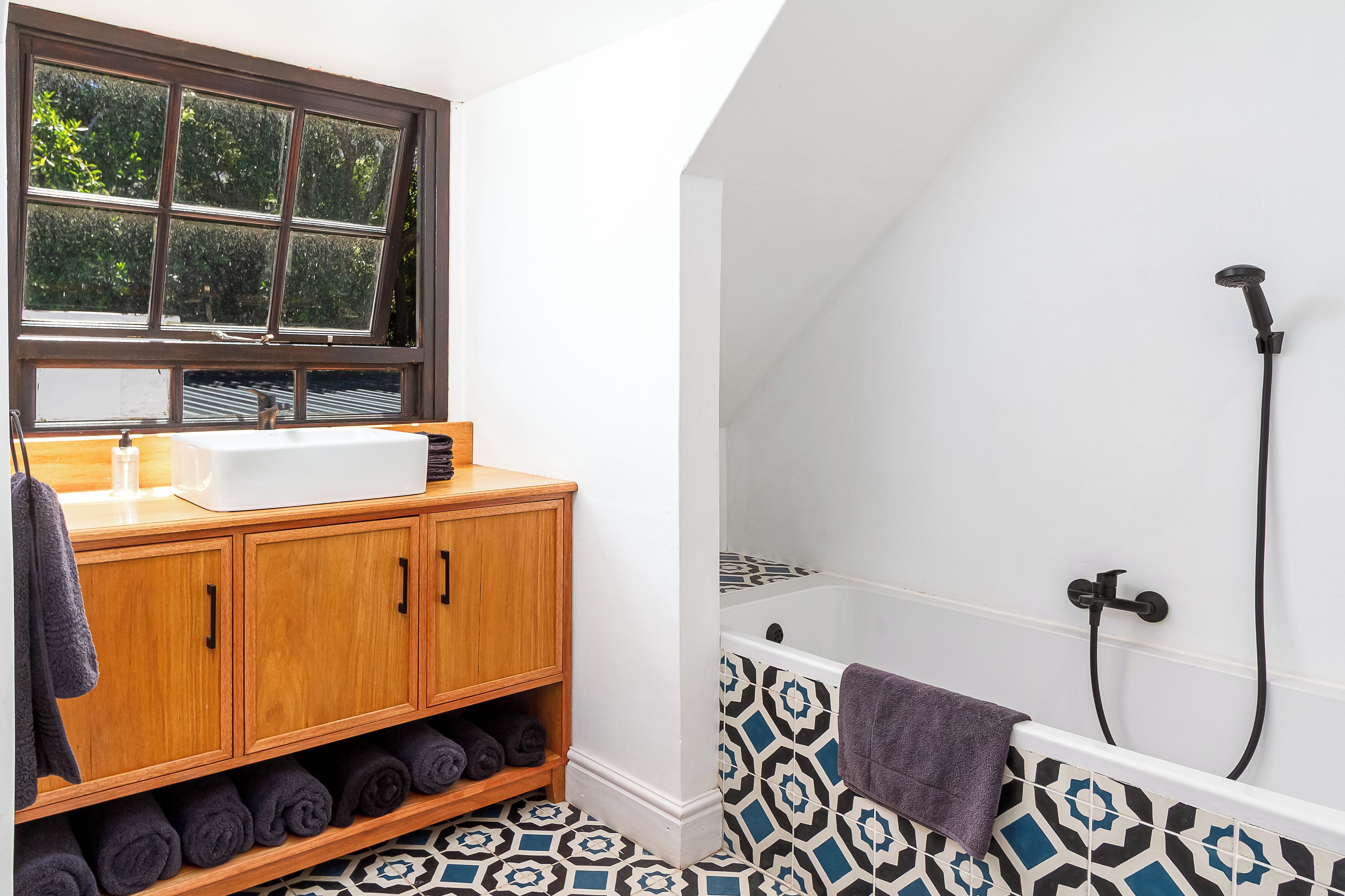 A bathroom with a wooden vanity, a white sink, and a patterned bathtub.