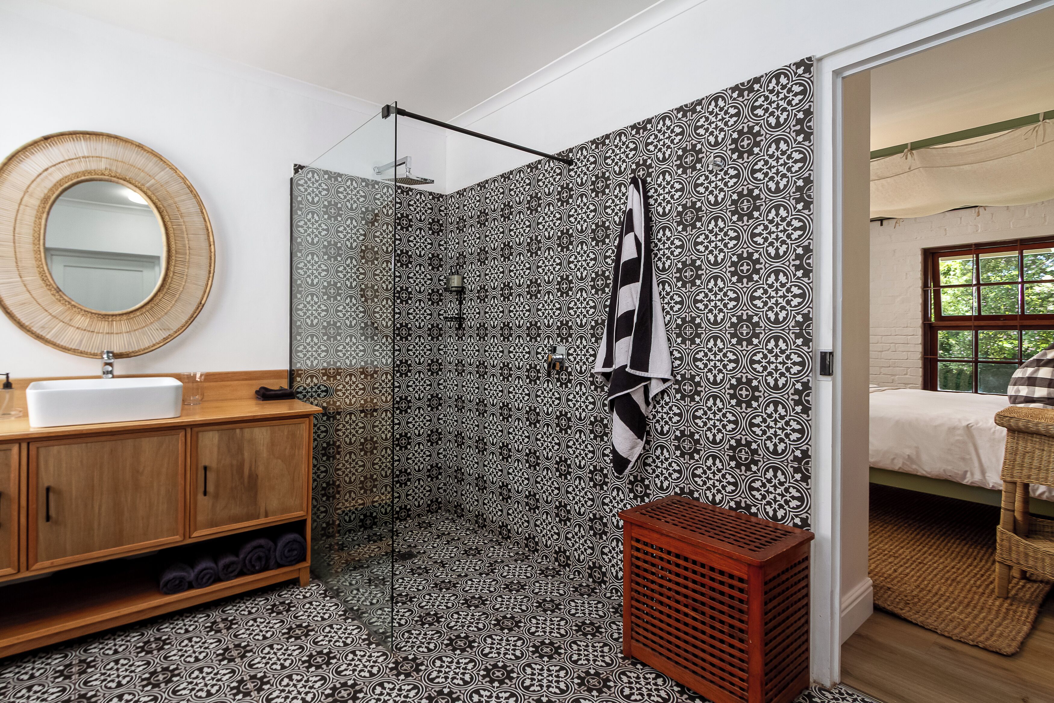 A bathroom with a patterned tile wall, a wooden vanity with a sink, a mirror, and a shower area.