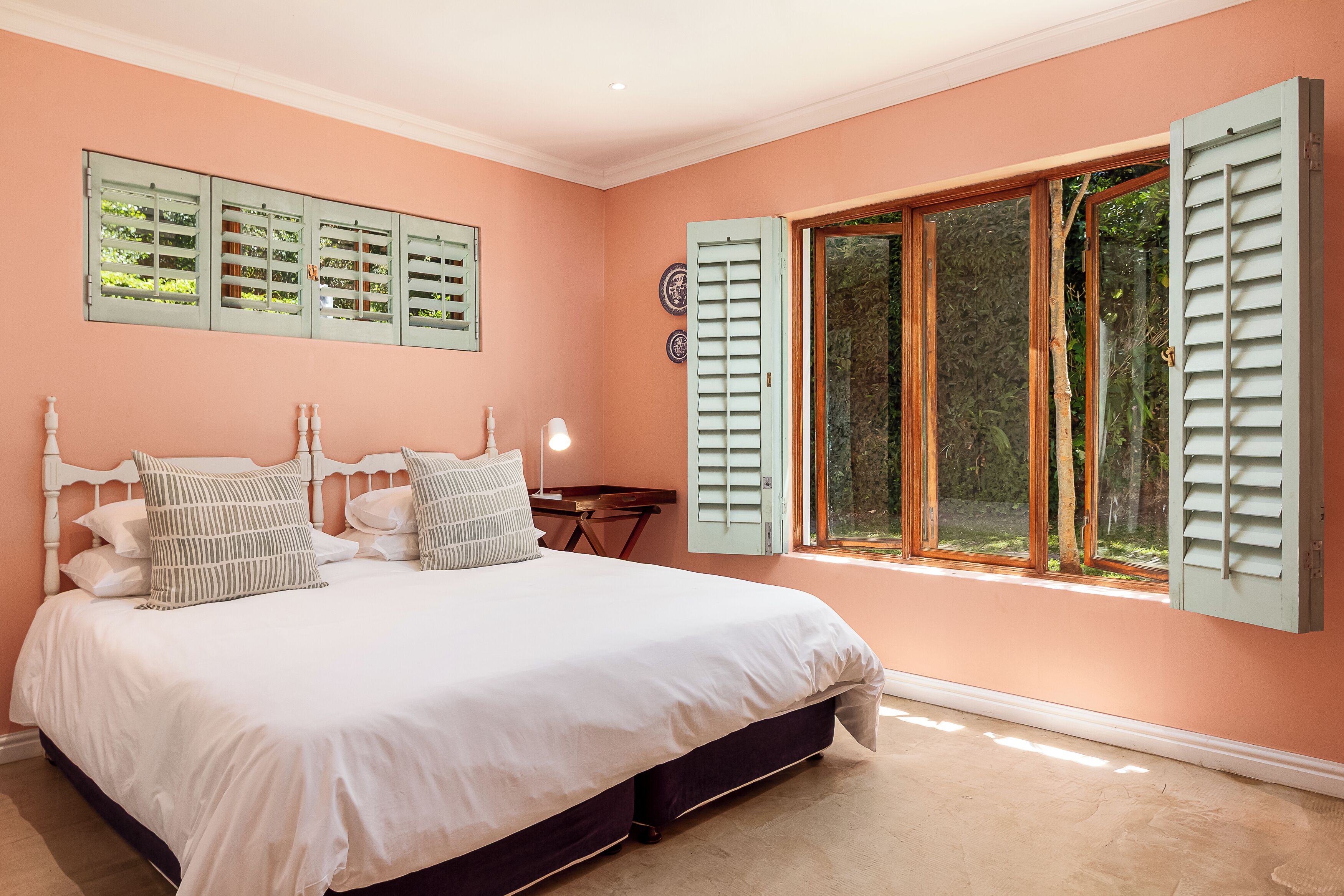 Un dormitorio con una cama grande, una mesita de noche, una lámpara y una ventana con contraventanas.