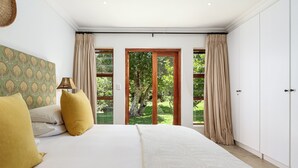 Une chambre avec un grand lit, des rideaux de couleur beige et une vue sur la verdure.