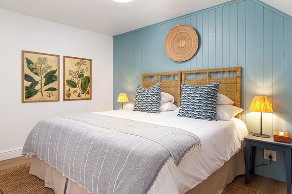 Une chambre à coucher comprenant un lit, deux lampes fixées au mur et deux illustrations botaniques encadrées.