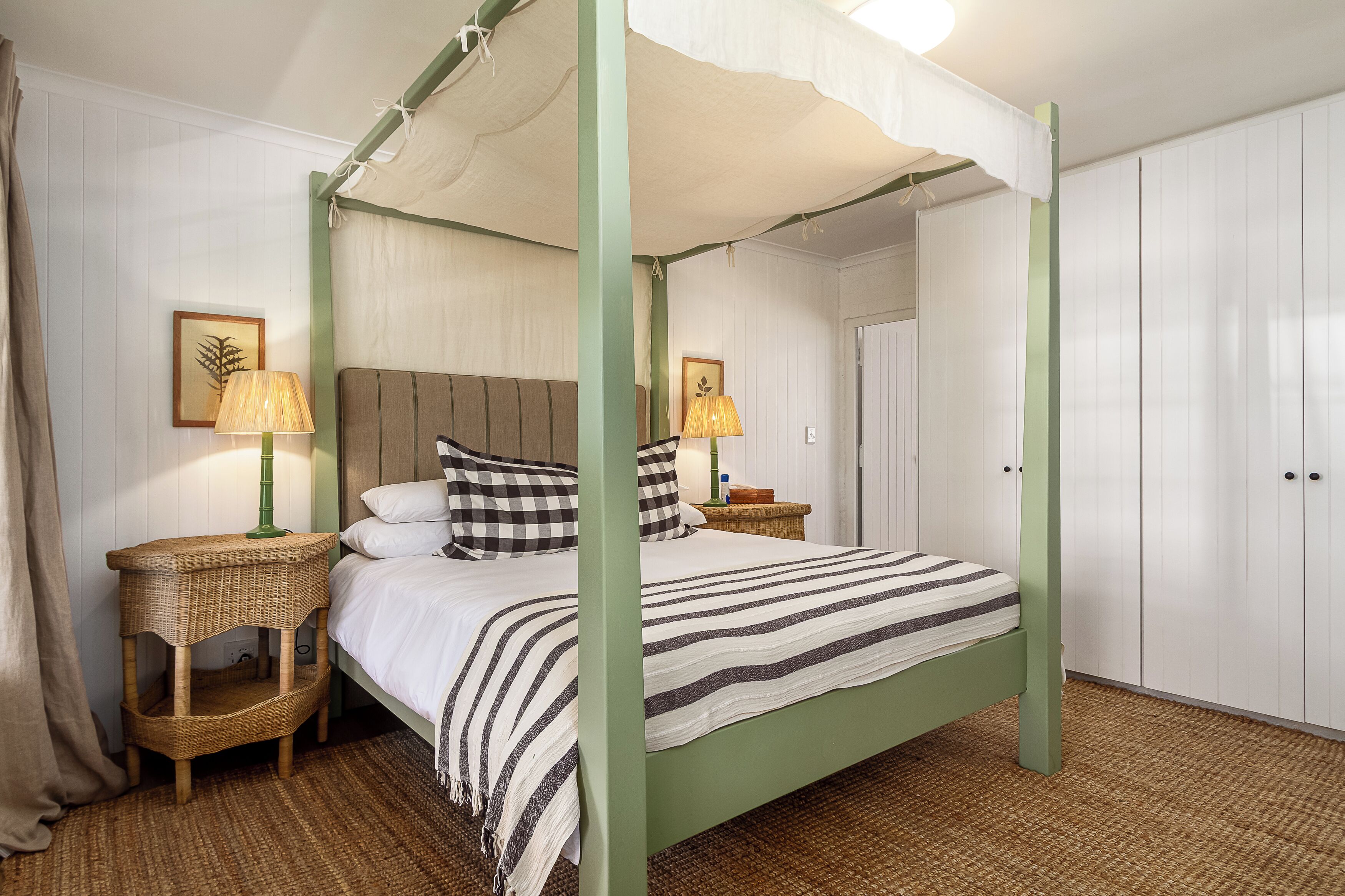 A four-poster bed with a green frame, two bedside tables with lamps, and a white wall with a framed picture.