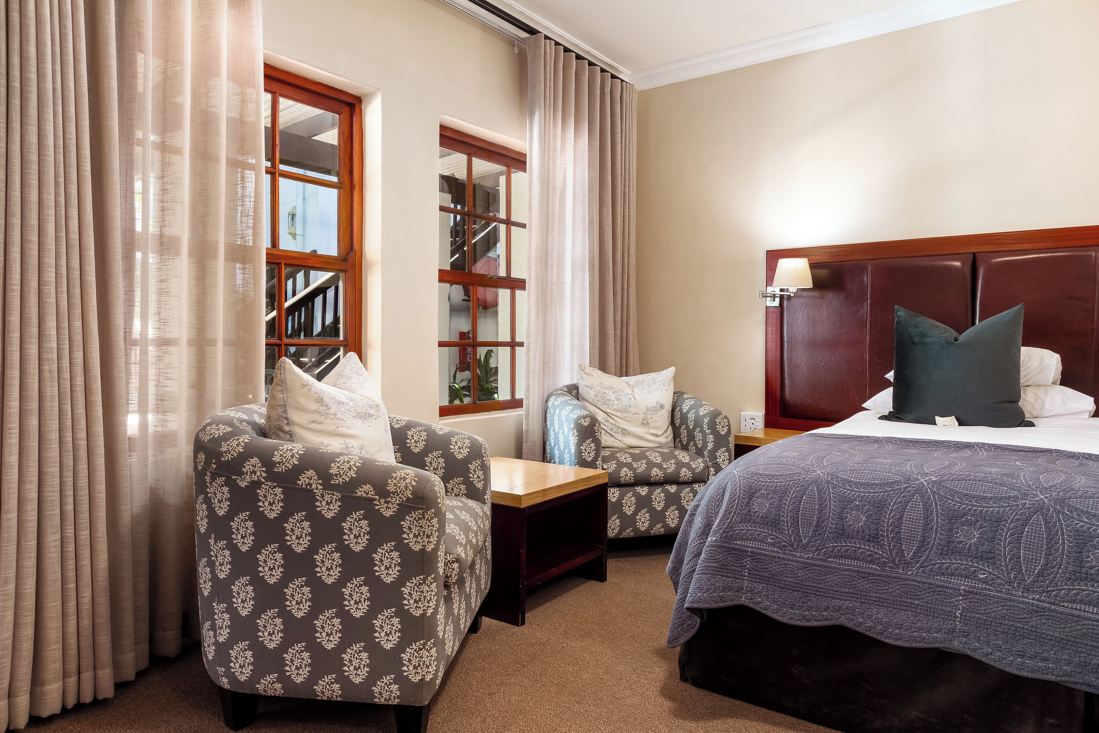 A hotel room with a bed, two armchairs, a small table, and a window with curtains.