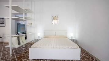 Ein Schlafzimmer mit einem weißen Bett, einem Schreibtisch mit Computer und einem Bücherregal.