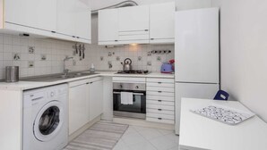 Une cuisine compacte avec des meubles blancs, un lave-linge encastré, une cuisinière et un réfrigérateur.