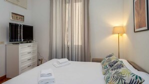Une chambre d’hôtel avec un lit, un téléviseur posé sur une commode, une lampe et une fenêtre avec des rideaux.