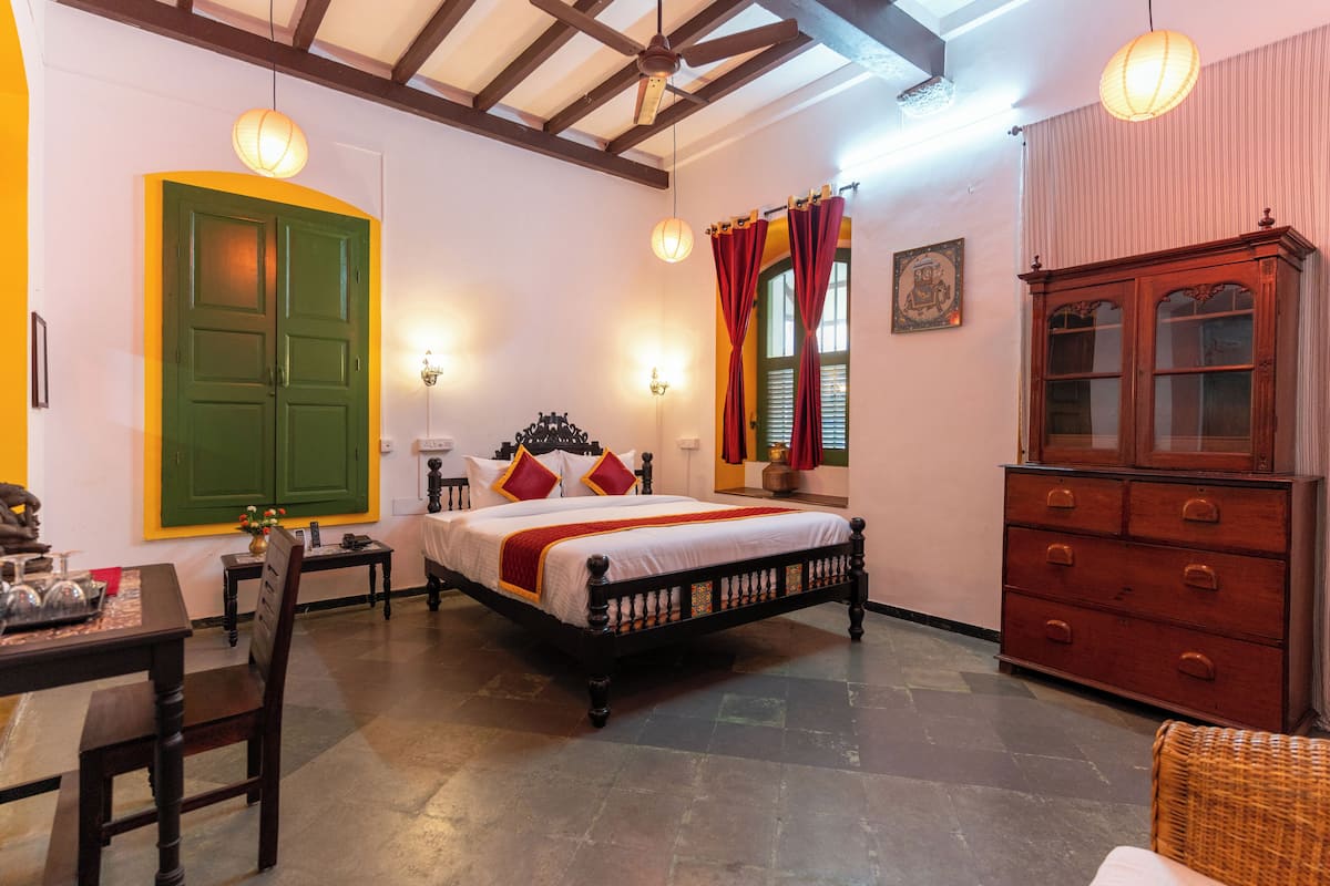 A room with a bed, a wooden cabinet, a table with chairs, and a wall-mounted shelf.