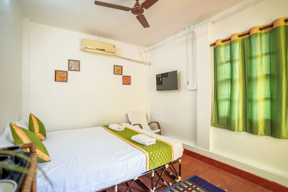 A room with a bed, a chair, a television, and a window with curtains.