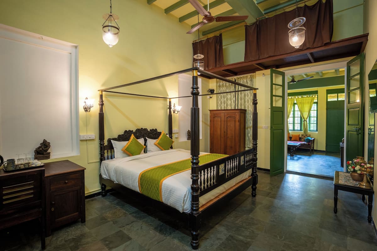 A four-poster bed with a wooden frame and green bedding, a wooden nightstand, a dresser, and a small table with a vase.