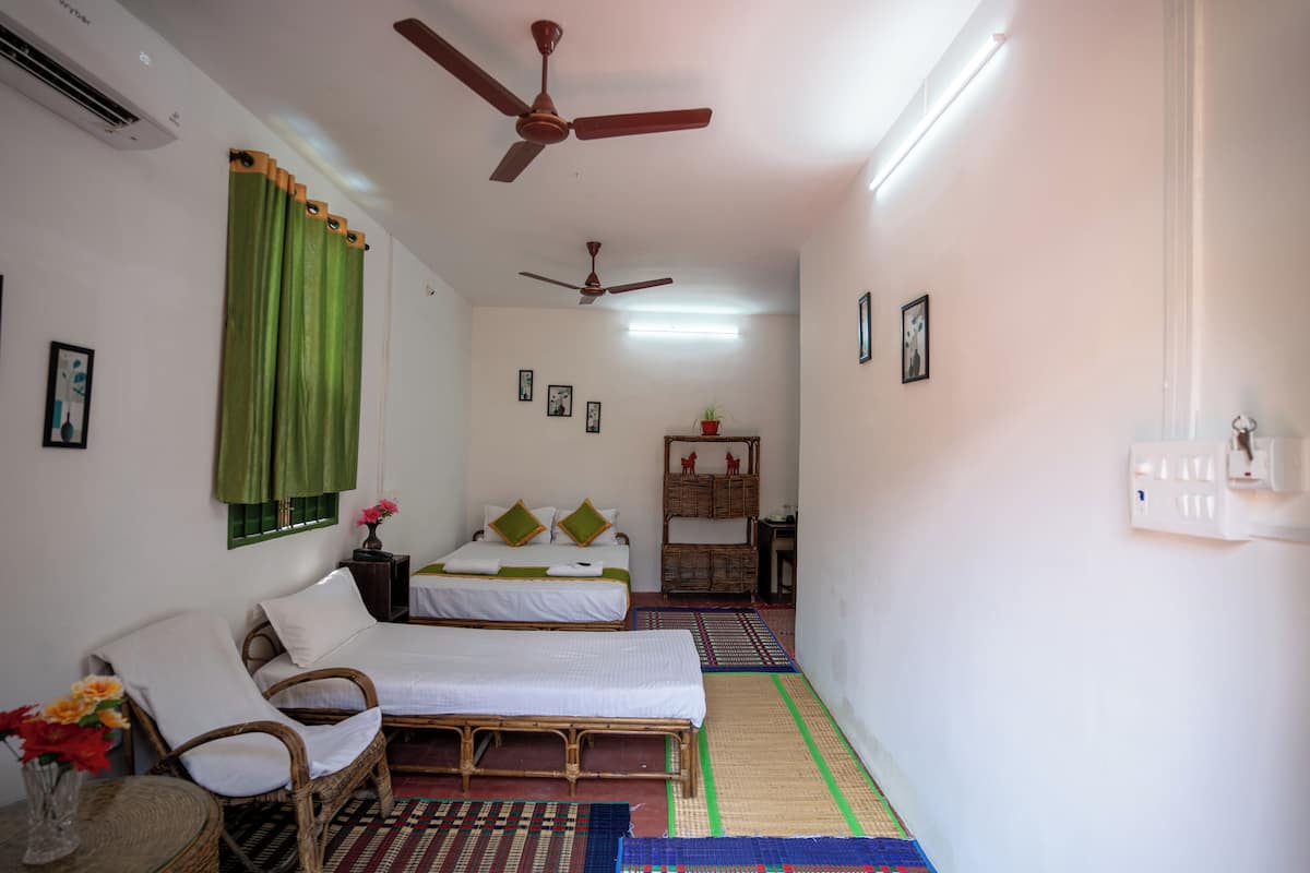 A room with two single beds, a chair, a small table with flowers, and a ceiling fan.