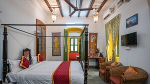 A four-poster bed with a red and white bedspread, a wooden headboard, and two wicker armchairs with red cushions. - Luigi Villa (Puducherry)