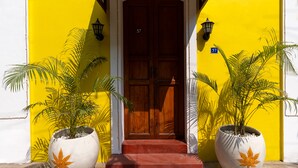 A building entrance with a wooden double door, a red carpet, and two large potted plants with yellow leaves. - Luigi Villa (Puducherry)