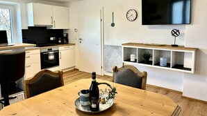 A modern kitchen with white cabinets, a built-in oven, and a dining area with a wooden table and chairs.