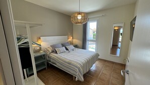 A bedroom with a bed, bedside tables, a hanging light fixture, a wardrobe, and a window with a view.