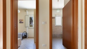 A hallway with wooden doors, a tiled floor, and a view into a room with a bed and a window. - 3846 Villetta Le Largure A by Barbarhouse (Melendugno)