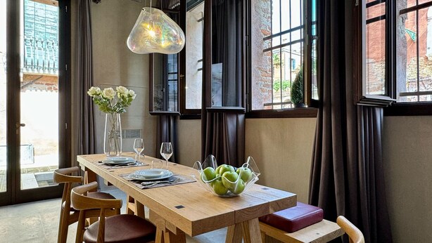 A dining area with a wooden table, chairs, a vase with flowers, and a bowl of green apples. - Spezier Canal View (with common terrace) (Venecia)