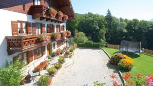 A traditional chalet with wooden balconies and flower boxes, a gravel driveway, and a trampoline in the yard. - Ferienwohnung Zuhaus - 2 Personen, 35 qm, Terrasse mit Bergblick (Bad Reichenhall)