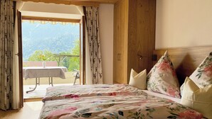 A bedroom with a bed, floral bedding, and a view of a balcony with a table and chairs. - Ferienwohnung Zuhaus - 2 Personen, 35 qm, Terrasse mit Bergblick (Bad Reichenhall)