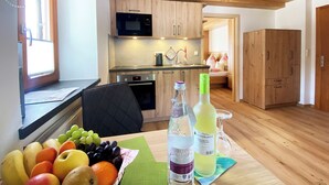A modern kitchen with wooden cabinets, a microwave, and a sink. There is a dining table with a fruit bowl and bottles of water. - Ferienwohnung Zuhaus - 2 Personen, 35 qm, Terrasse mit Bergblick (Bad Reichenhall)