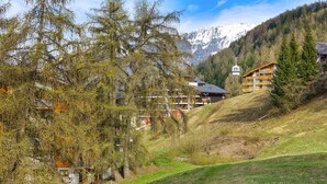 A mountain lodge with multiple buildings, a ski lift, and a view of snow-capped mountains. - Ambassador II n°10 - 4 pers - près des pistes (Haute-Nendaz)