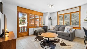 A modern living room with a wooden floor, a round coffee table, a grey sofa, and a cowhide rug. - Ambassador II n°10 - 4 pers - près des pistes (Haute-Nendaz)