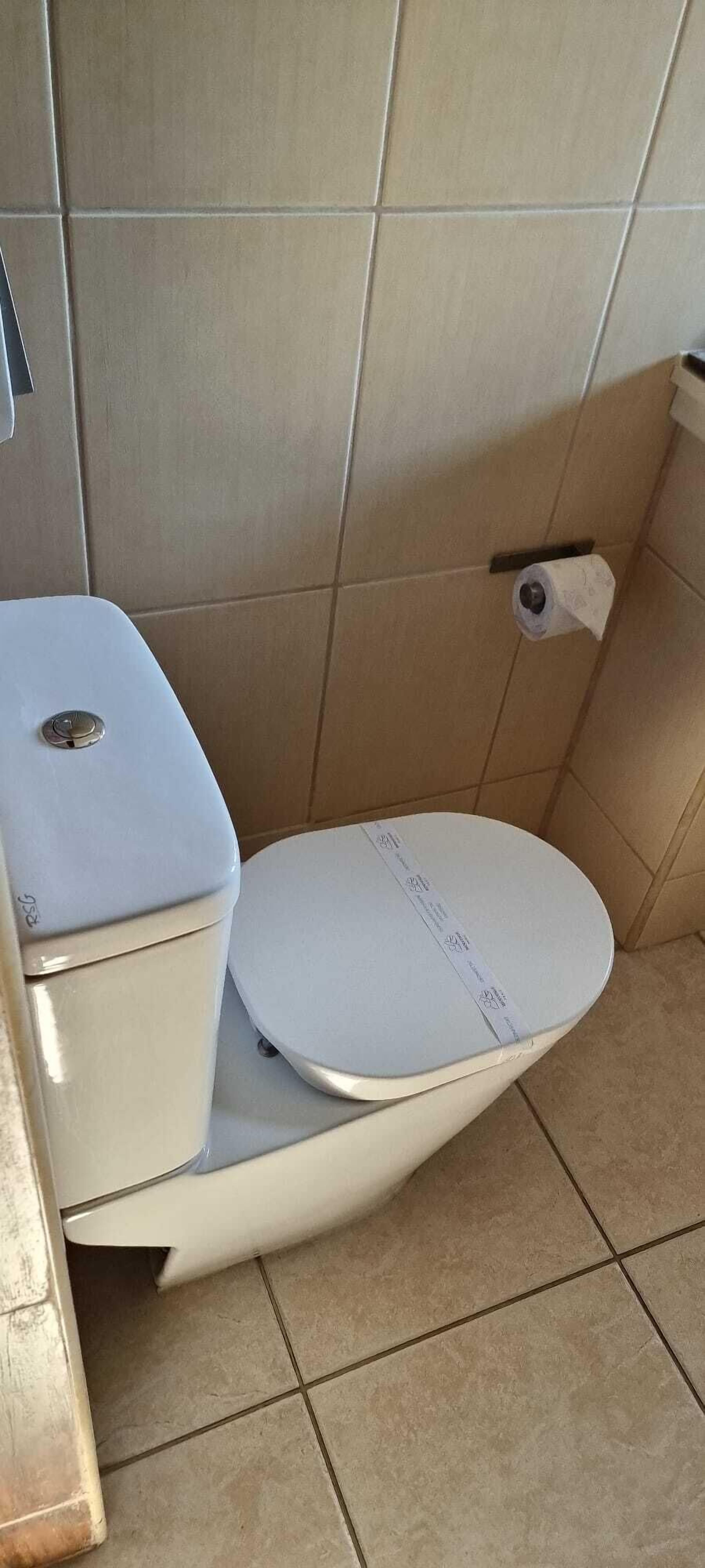 A standard toilet with a white seat and lid, a toilet paper holder on the wall, and a tiled floor.