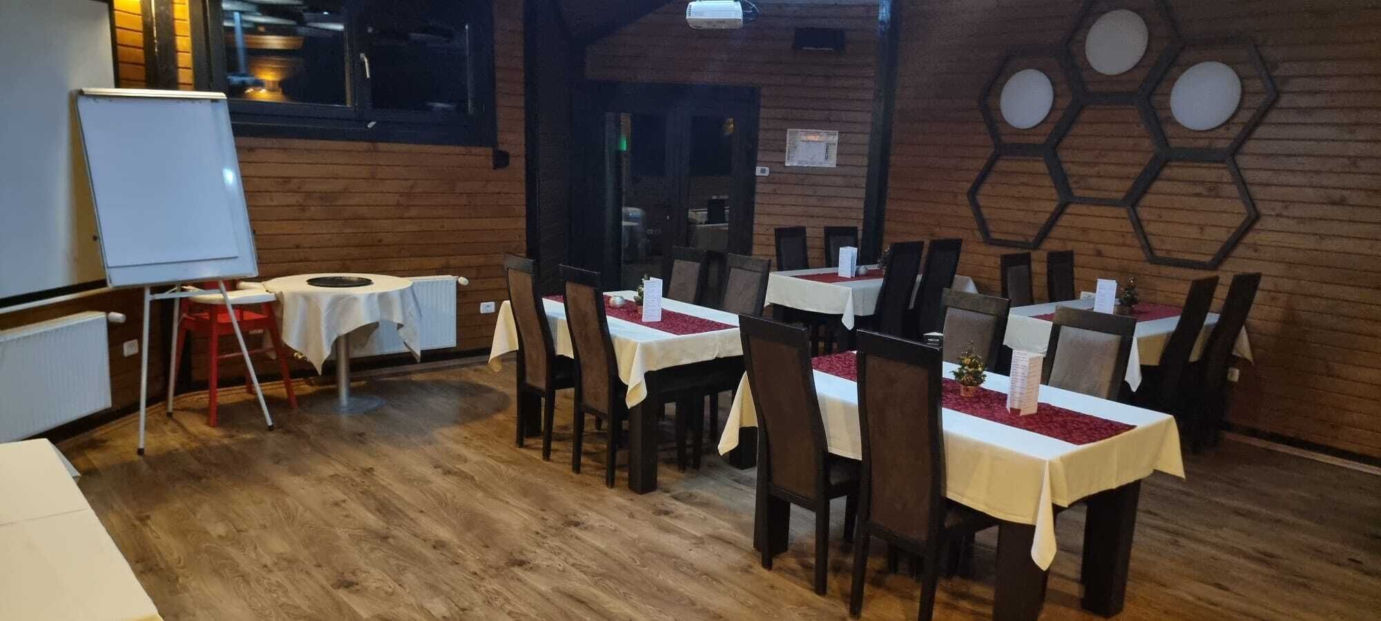 A restaurant with wooden flooring and tables set with white tablecloths and red centerpieces.