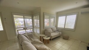 Ein geräumiges Wohnzimmer mit einer großen Couch, einem kleinen Tisch und einem Fenster mit Jalousien.