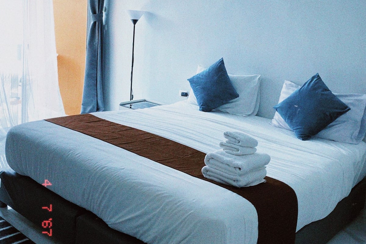 Une chambre d’hôtel avec un lit, des oreillers, une lampe et une fenêtre avec des rideaux.