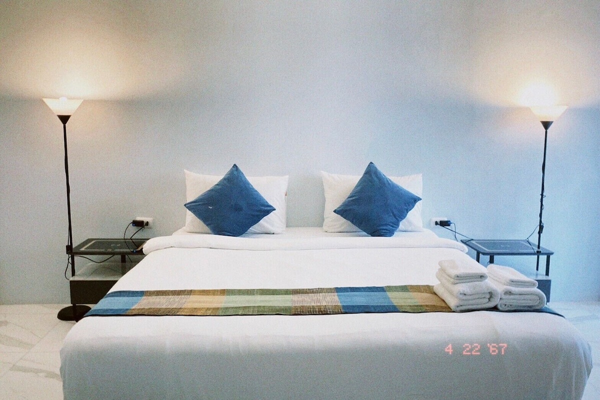 Une chambre d’hôtel avec un lit bien fait, deux lampes de chevet, une petite table avec une lampe et une serviette pliée posée sur le lit.