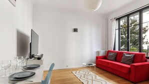 Una sala moderna con comedor, un sofá rojo y ventanas amplias.