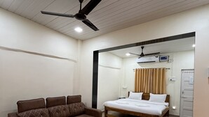 A hotel room with a brown sofa, a wooden bed, a ceiling fan, and an air conditioning unit. - O Nest Beach Front Villa (Alibag)