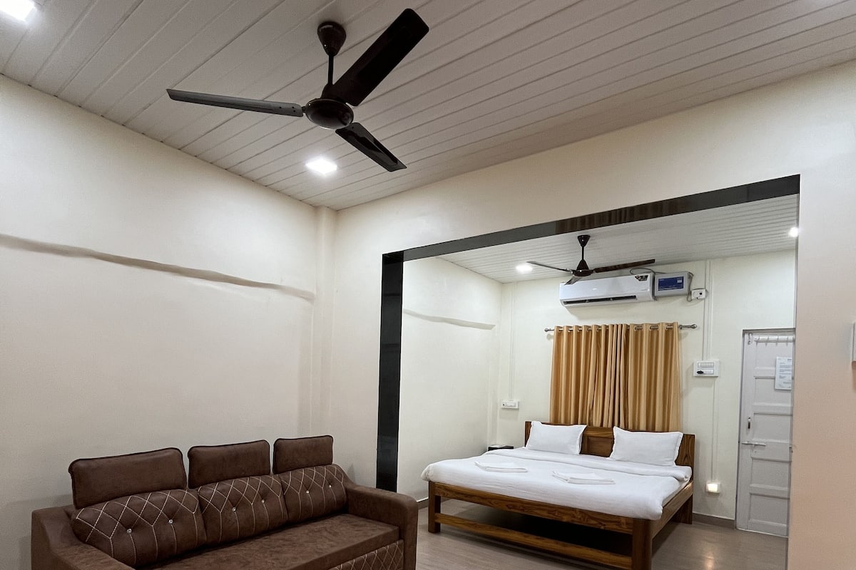 A hotel room with a brown sofa, a wooden bed, a ceiling fan, and an air conditioning unit.