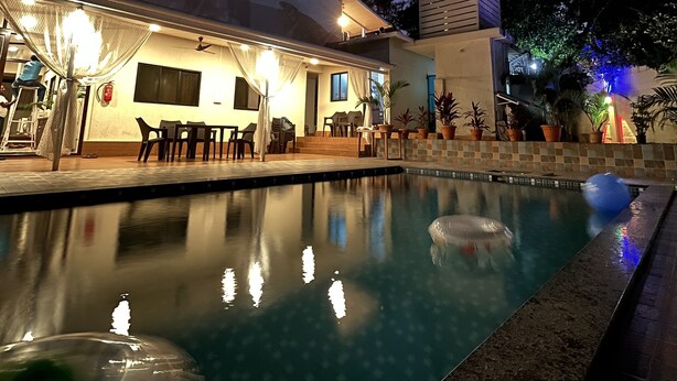 A modern poolside area with a clear pool, outdoor seating, and a covered patio area. - O Nest Beach Front Villa (Alibag)