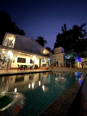 Un área moderna junto a la piscina con piscina cristalina, mobiliario exterior y un porche cubierto.