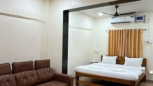 A hotel room with a bed, a brown sofa, a ceiling fan, and an air conditioning unit. - O Nest Beach Front Villa (Alibag)