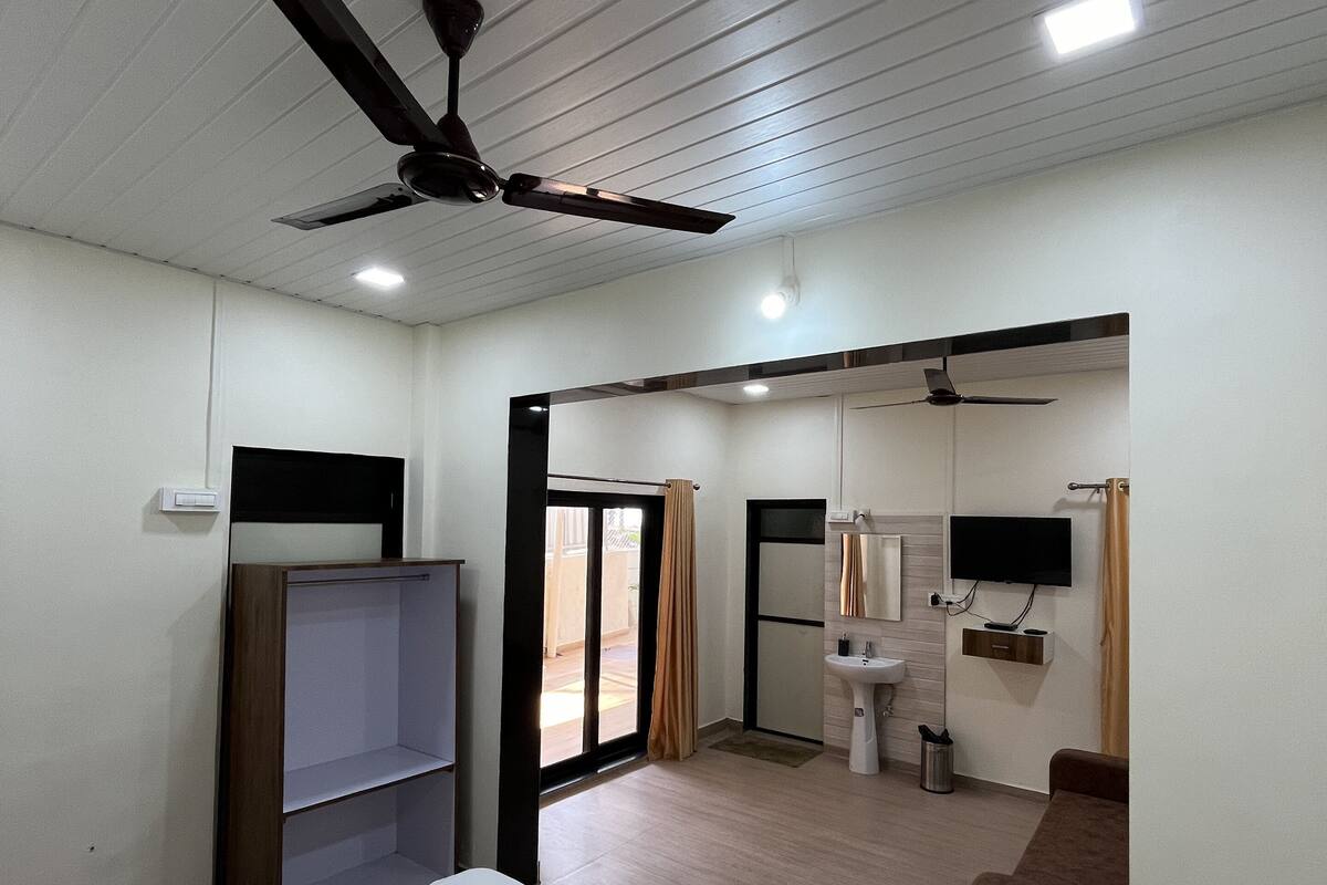 A hotel room with a bed, a ceiling fan, a TV, a sink, and a mirror.
