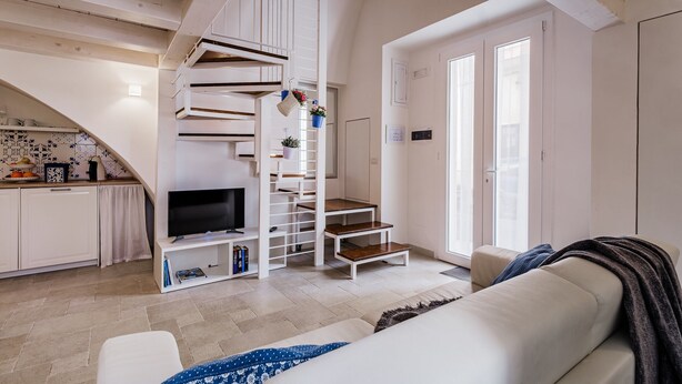 A modern living room with a staircase, a TV, and a sofa. - Holiday Apartment in Puglia near the beaches (Polignano a Mare)