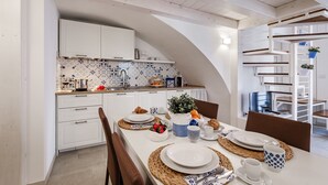 A modern kitchen with white cabinets, a tiled backsplash, and a dining area with a long table set for two. - Holiday Apartment in Puglia near the beaches (Polignano a Mare)