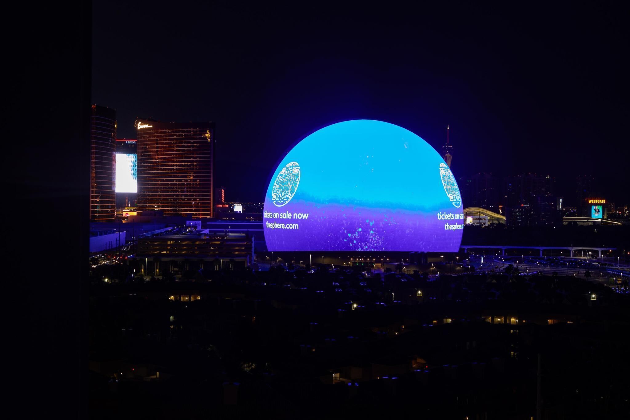 Une grande structure en forme de dôme, illuminée, avec un écran numérique affichant des publicités pour la vente de billets.