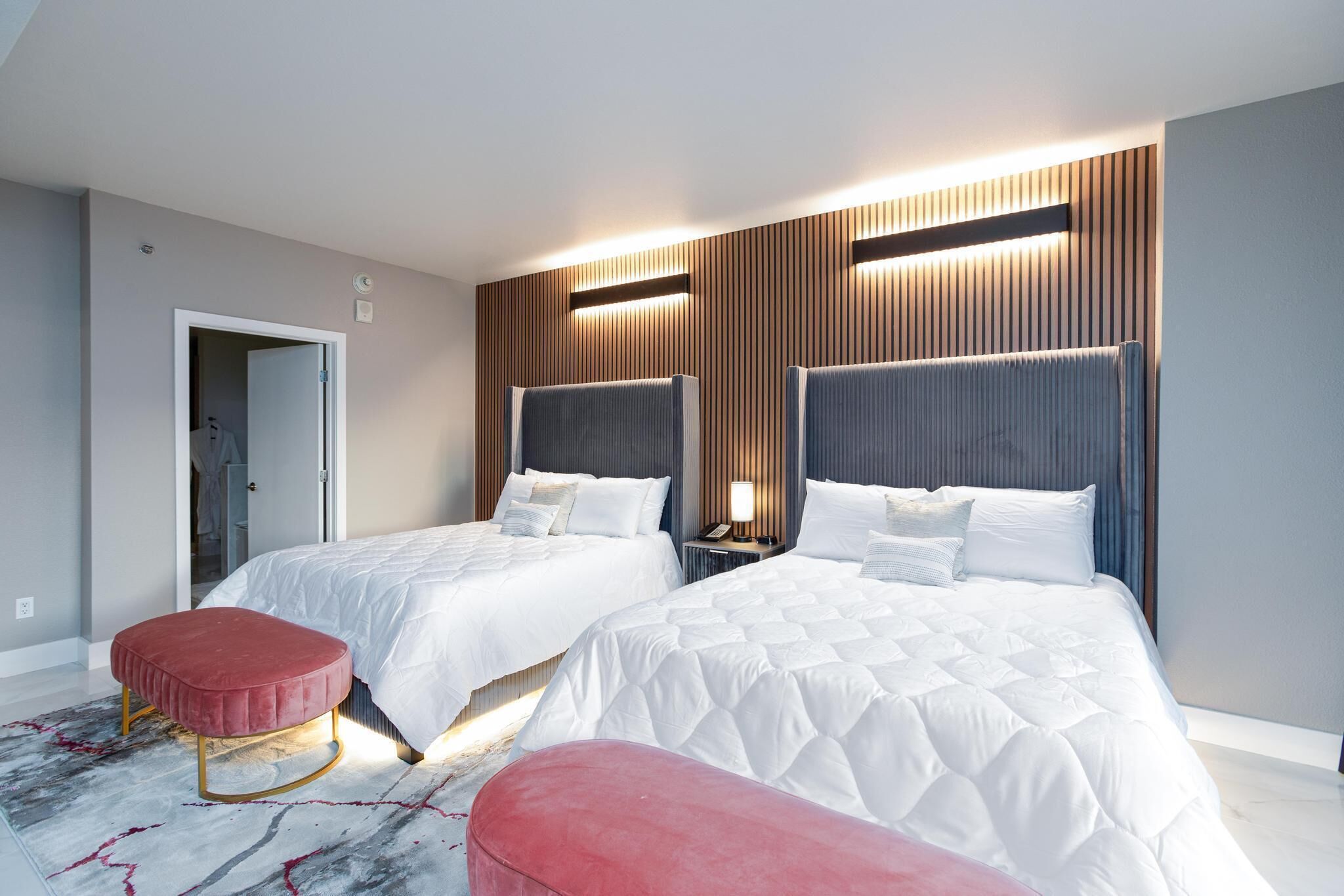 Une chambre d’hôtel moderne avec deux lits, un pouf rouge et une table de chevet avec une lampe.