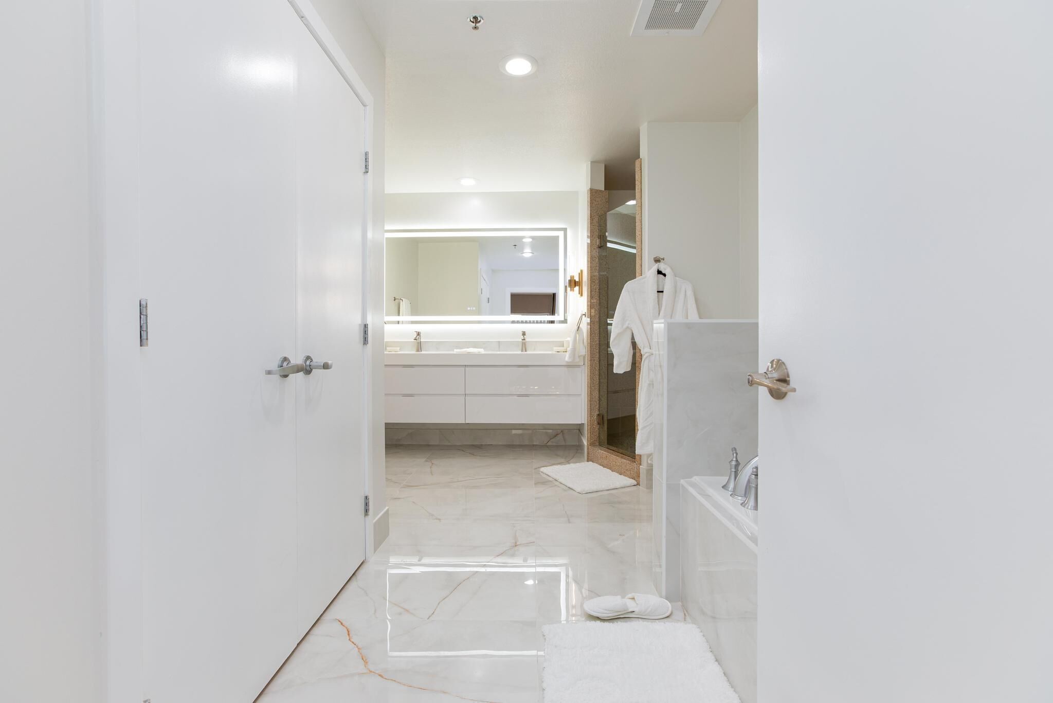 A modern bathroom with a large mirror, white fixtures, and a marble floor.