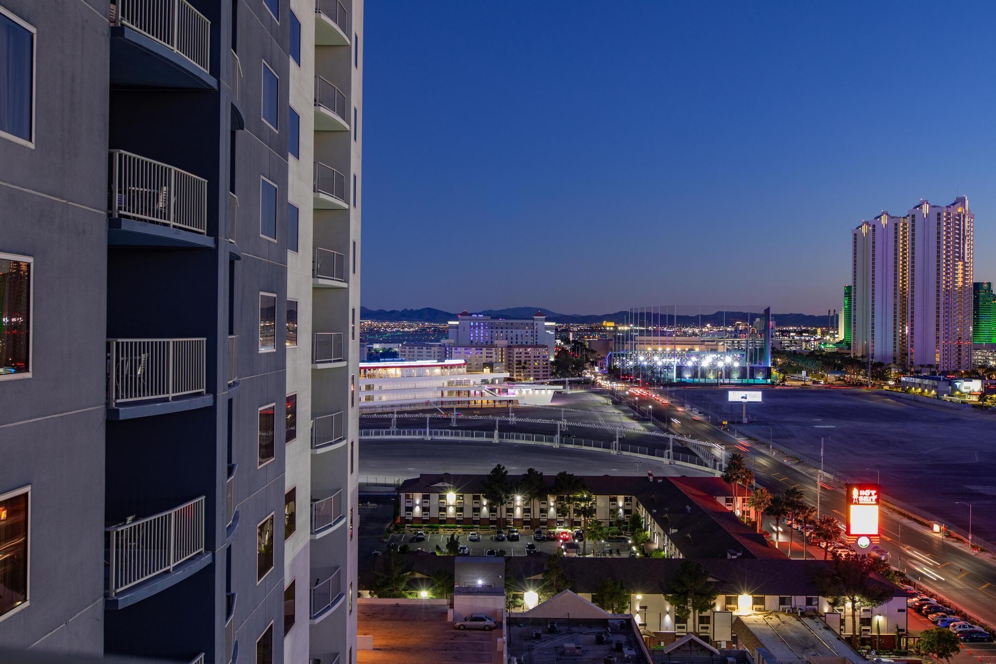 A high-rise building with multiple balconies and a parking area in the foreground.