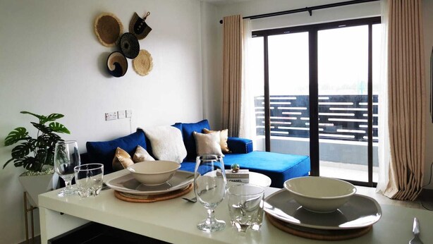 A modern living room with a sofa, dining table set with plates, glasses, and a small plant. - Lux Suites Enkang Apartments Ngong Road (Nairobi)