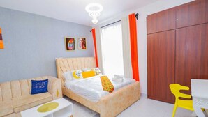 A bedroom with a bed, a sofa, a small table, a chair, and a wardrobe. - Lux Suites Enkang Apartments Ngong Road (Nairobi)