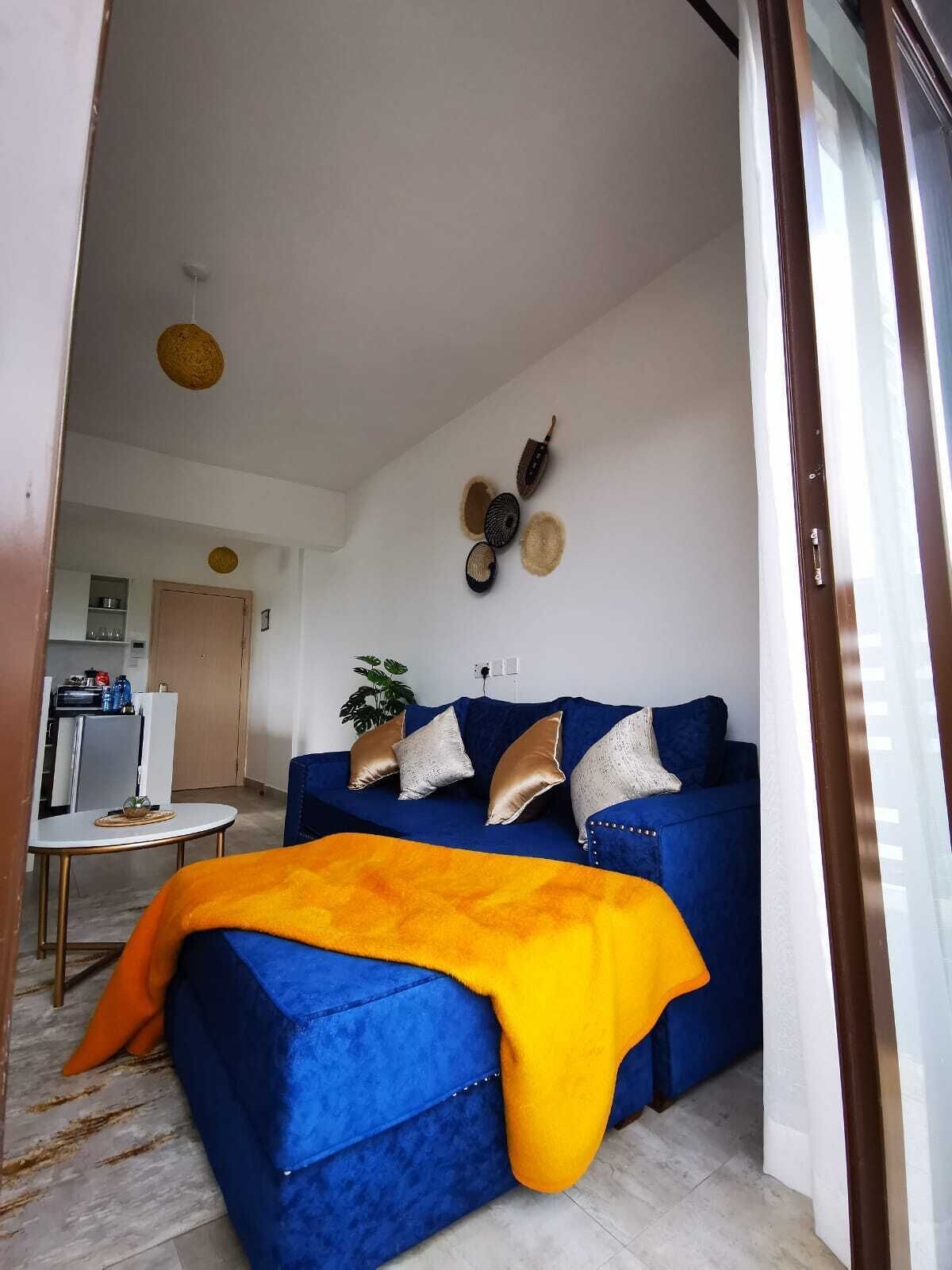 A modern living room with a blue sofa, a yellow throw blanket, and decorative wall art.